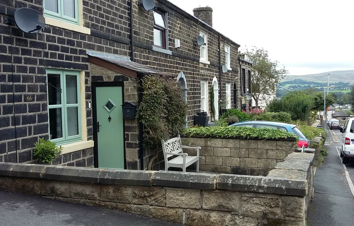 Stone terraced cottages with a green front door on Tanners Street in Ramsbottom, with hills beyond
