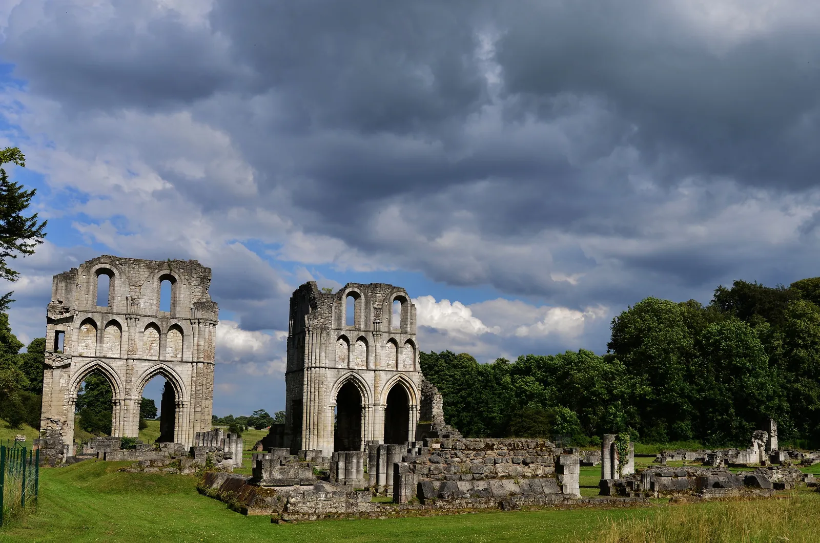 The ruined arches of Roche Abbey on green lawns under a stormy sky